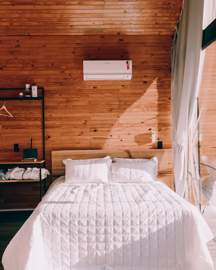 Interior do chalé, com paredes de madeira e cama de casal com colcha branca