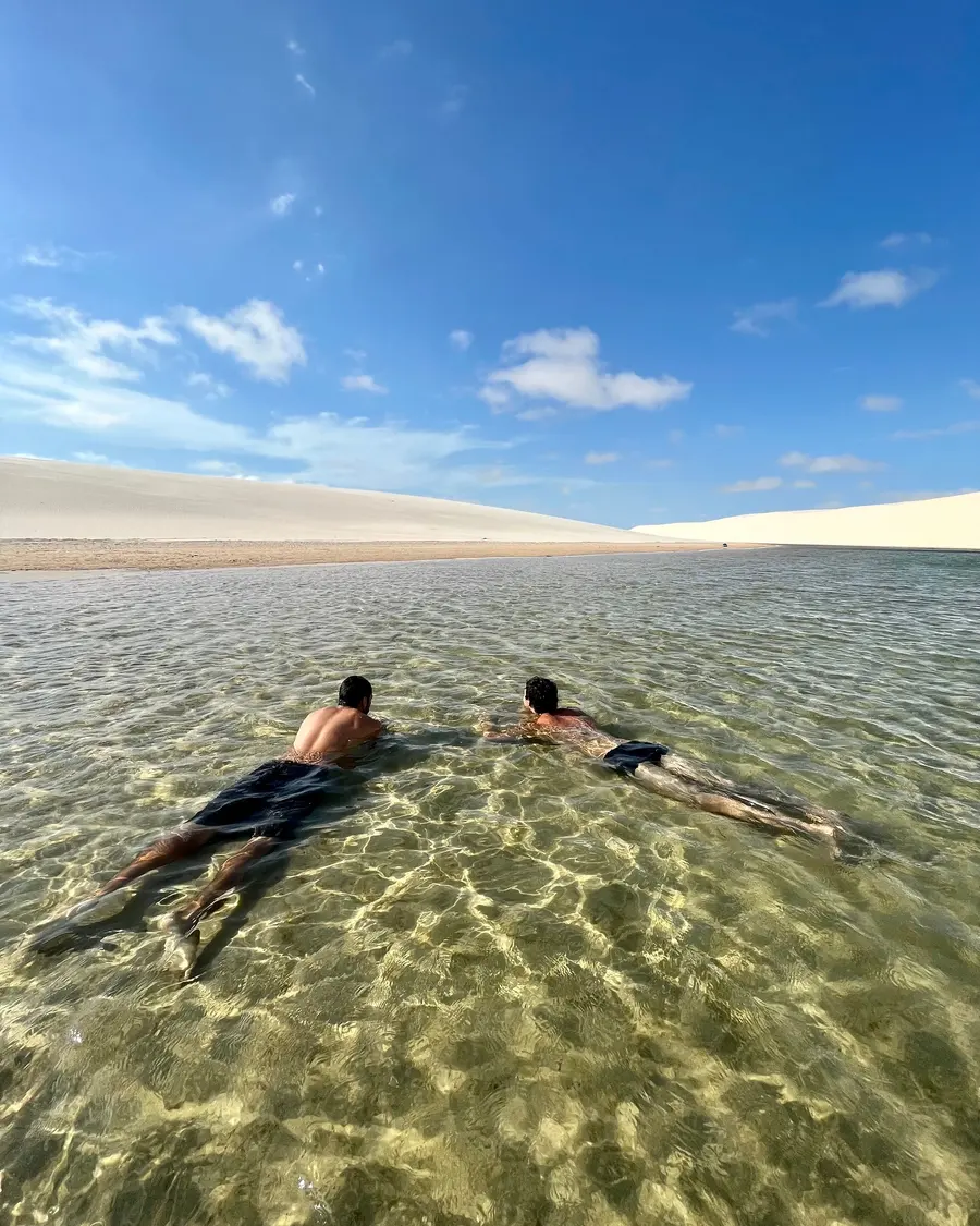 Duas pessoas boiando numa lagoa de água transparente entre as dunas