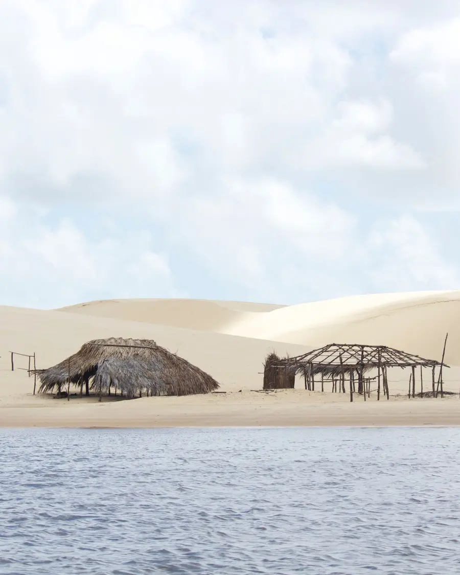 Cabanas de palha na beira da água, com dunas ao fundo