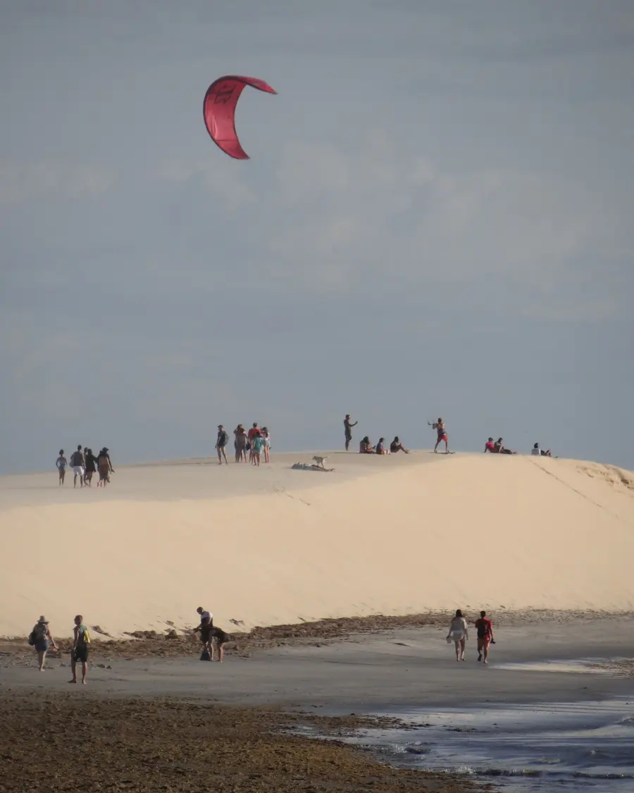 Pipa de kitesurf no céu acima de uma duna com pessoas