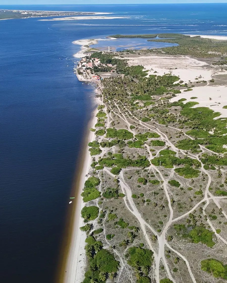 Vista aérea de um rio largo encontrando o mar, com dunas e vegetação na margem